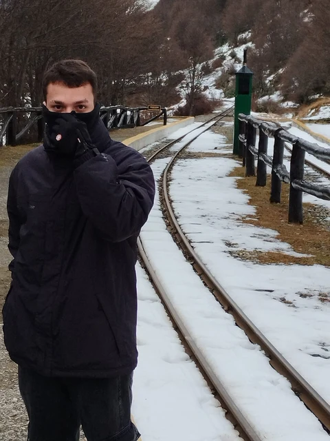 Vinicius Lucio de casaco preto, ao lado de trilhos em uma paisagem com neve.